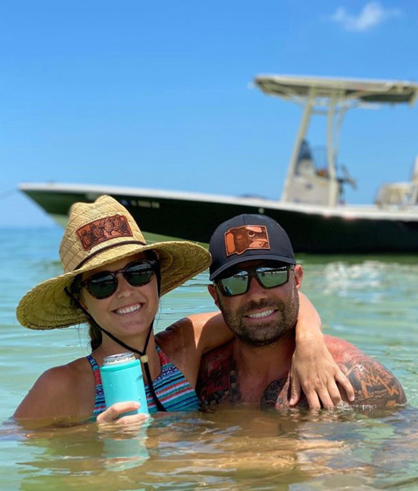 Photo of a straw lifeguard sun hat with a baby sea turtles patch and a Richardson 112 trucker hat with a detailed leather redfish tail patch, perfect for recreational saltwater fishermen seeking stylish, themed headgear for their fishing trips.