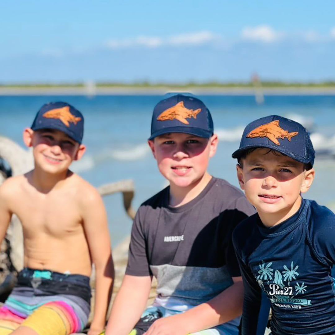 a photo showcasing a youth hat adorned with a genuine leather patch by Mokie Burns™ depicting a bull shark, the perfect outdoor sun hat accessory for kids who love the ocean and recreational fishing