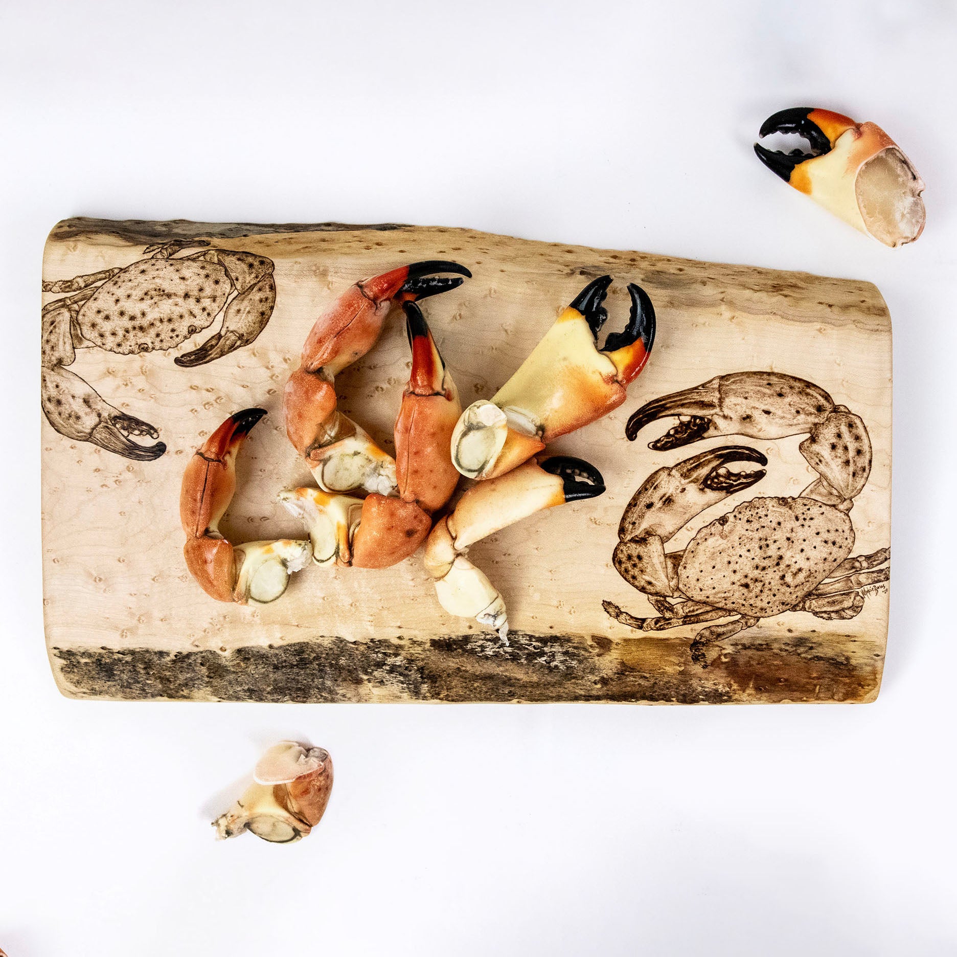 Live Edge serving tray with stone crab wood burned pyrography art on a white background, with fresh stone crab claws on the serving tray
